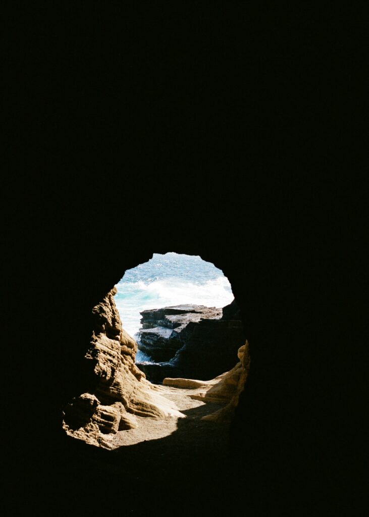 View from dark cave interior overlooking rugged rocks and swirling ocean waves with natural light Wallpaper