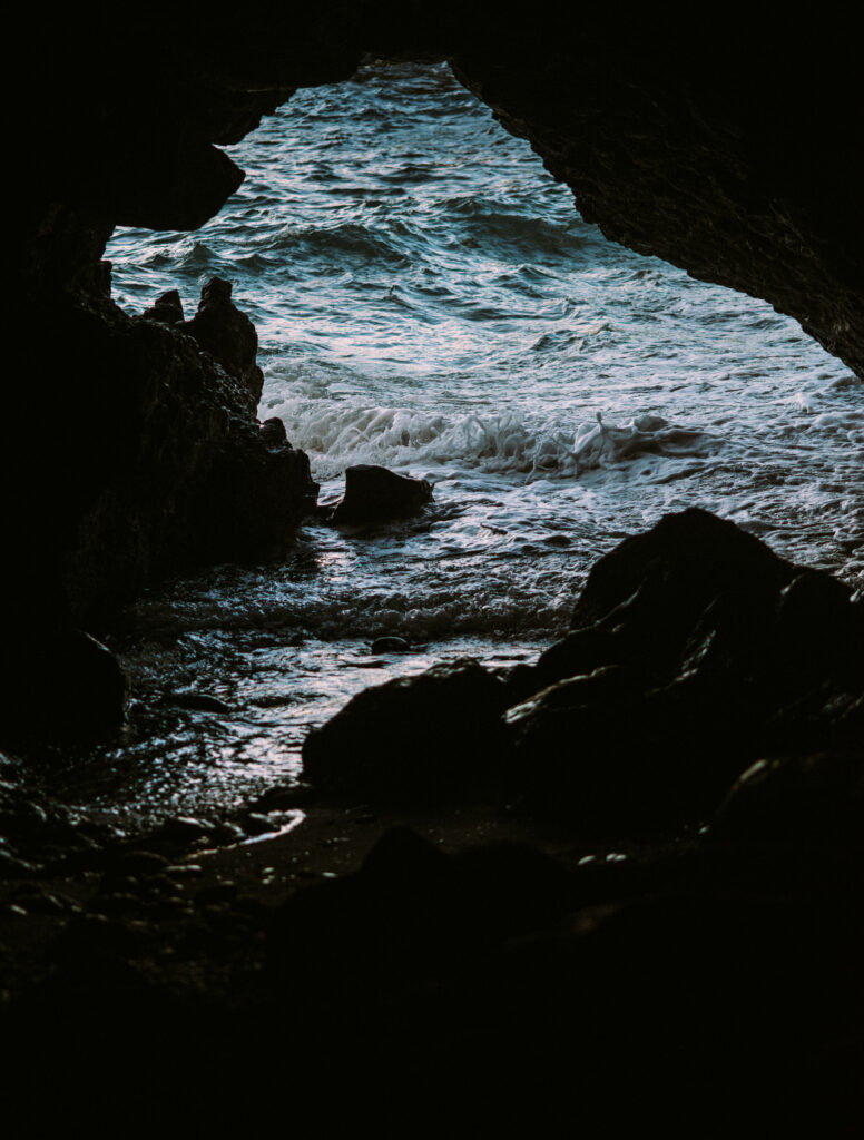 Dramatic cave view with jagged rocks and ocean waves crashing under natural light seascape wallpaper