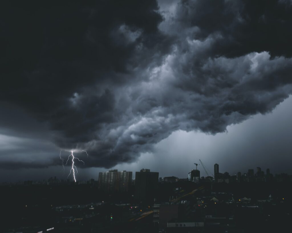 Stormy city skyline with dark clouds and bright lightning bolt illuminating the night sky Wallpaper