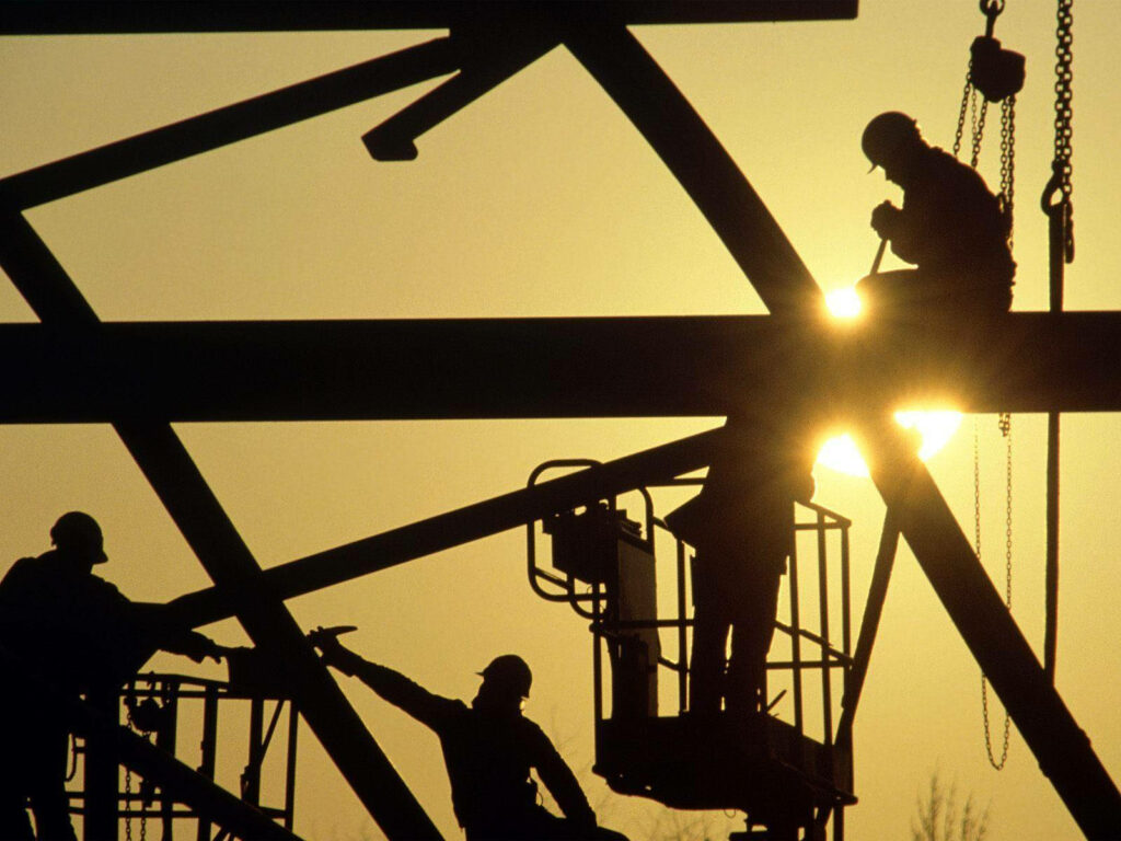 Silhouetted construction workers on steel beams at golden sunset industrial engineering wallpaper