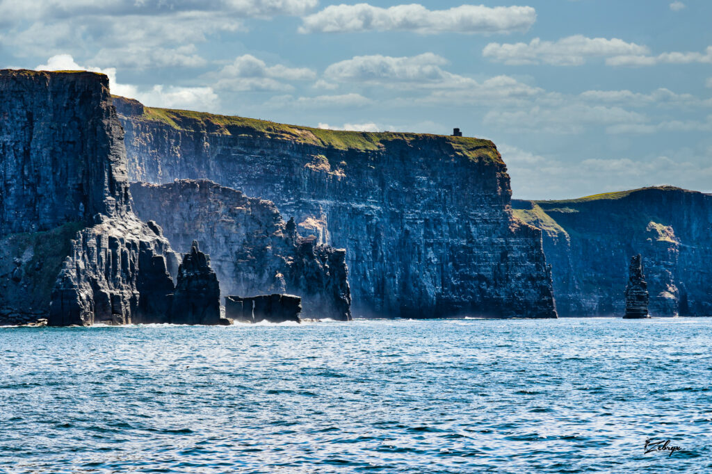 Dramatic cliffs and rocky formations rise above deep blue sea under soft cloudy sky wallpaper