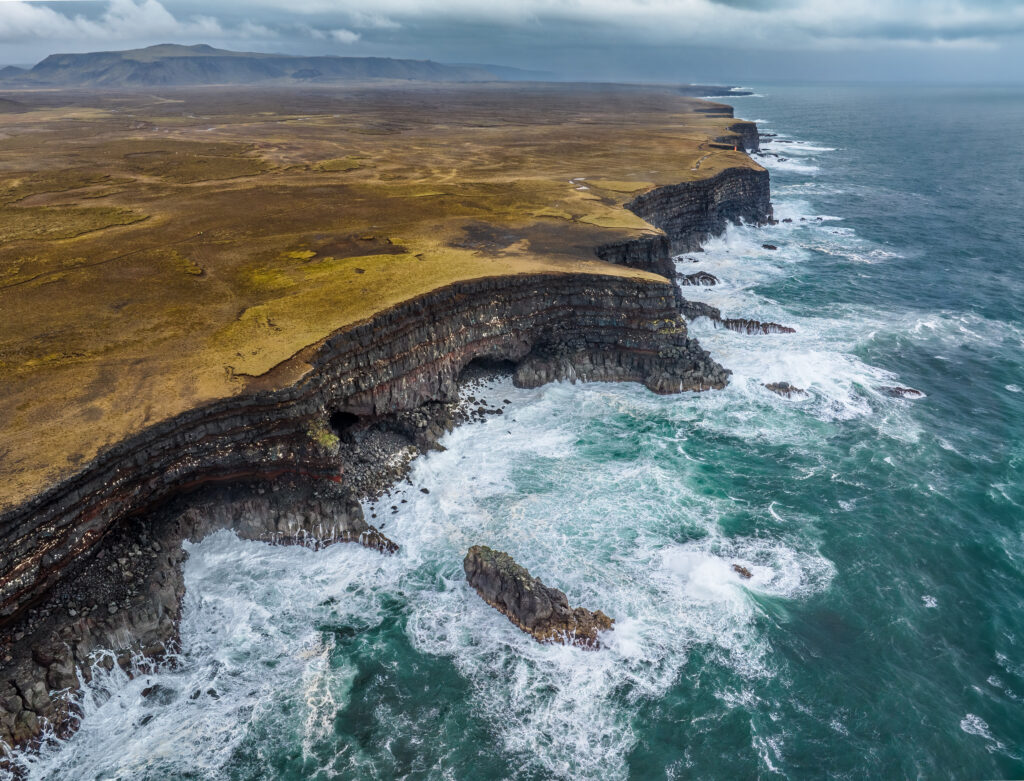 Dramatic cliffs and rocky formations above turbulent sea waves beneath cloudy sky wallpaper background