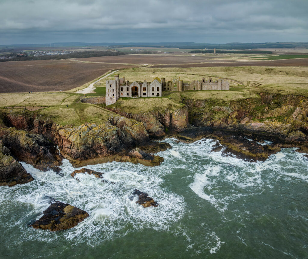 Dramatic stone castle on rugged cliff above crashing waves wild coastline moody wallpaper background