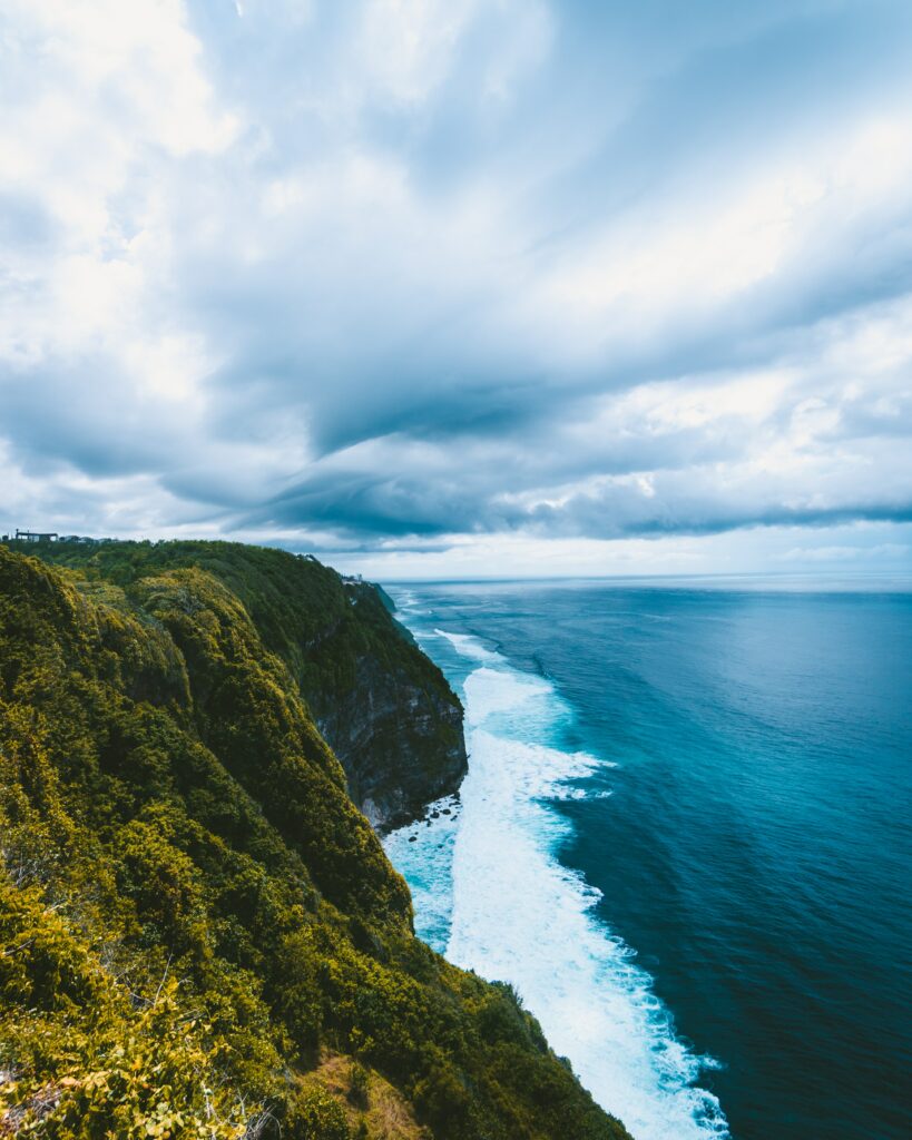 Dramatic green cliff overlooking blue sea with white surf and sweeping clouds serene wallpaper