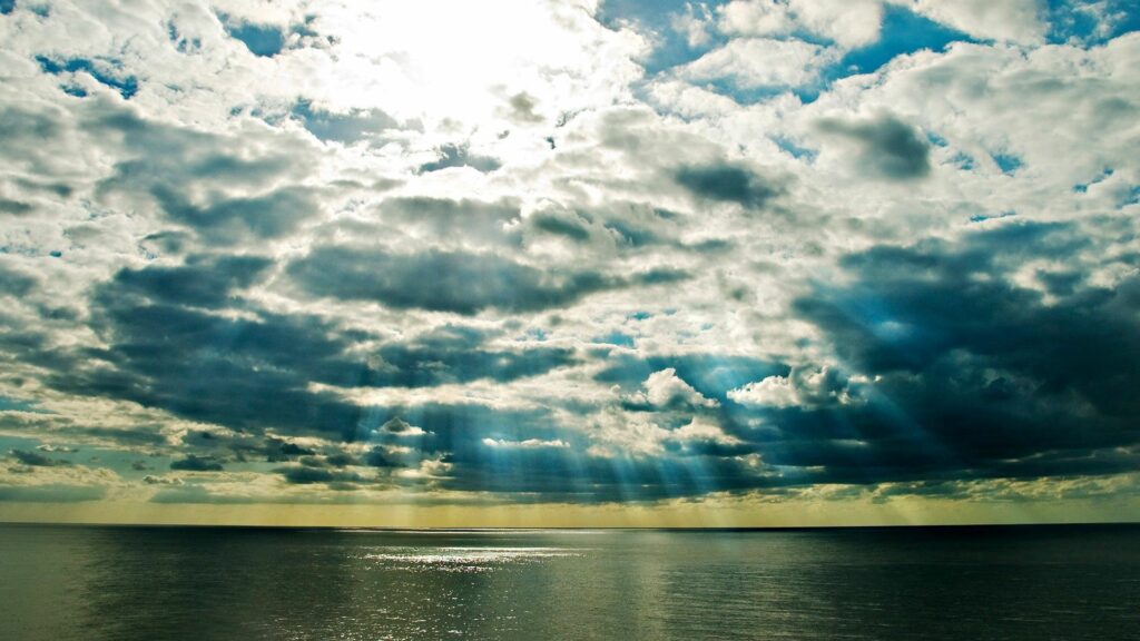 Dramatic clouds and sunlight beams over calm sea reflecting vibrant natural colors wallpaper
