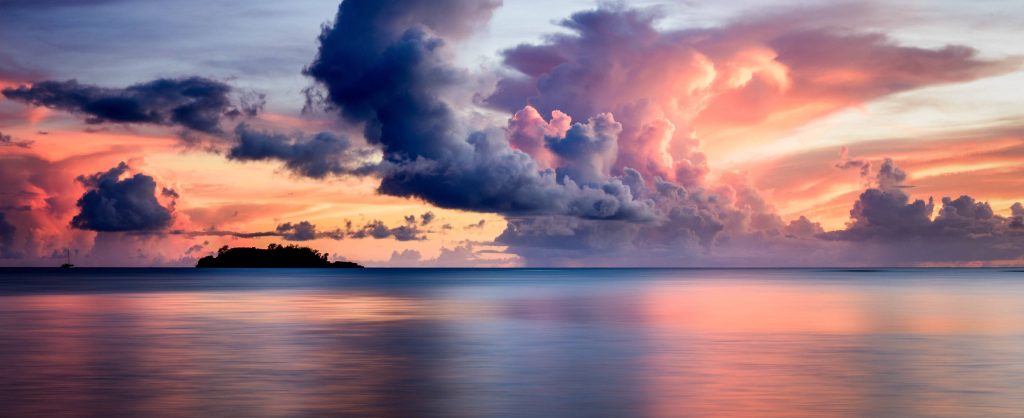 Dramatic cloudy sunset over calm sea with vibrant orange pink sky and distant island silhouette wallpaper