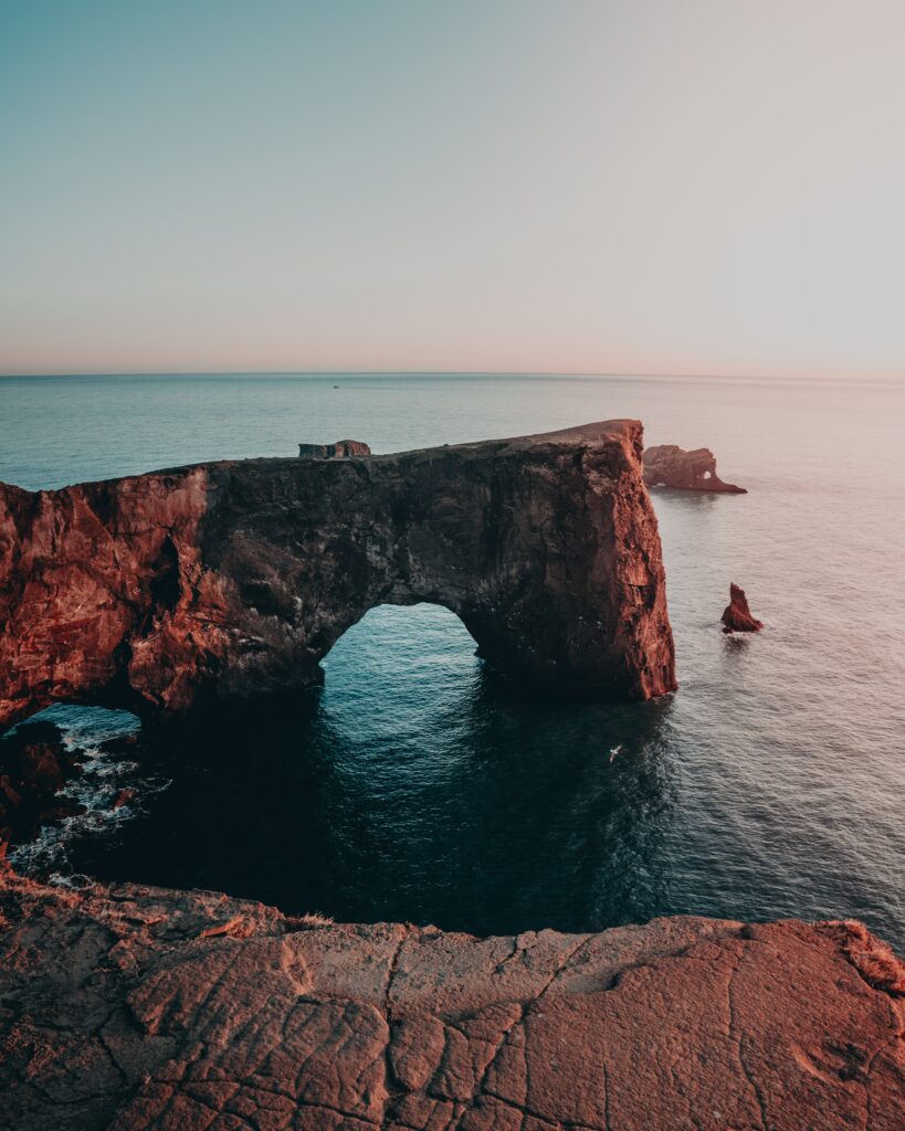 Dramatic sea landscape with rugged rocks and towering cliff arch in warm sunlight wallpaper