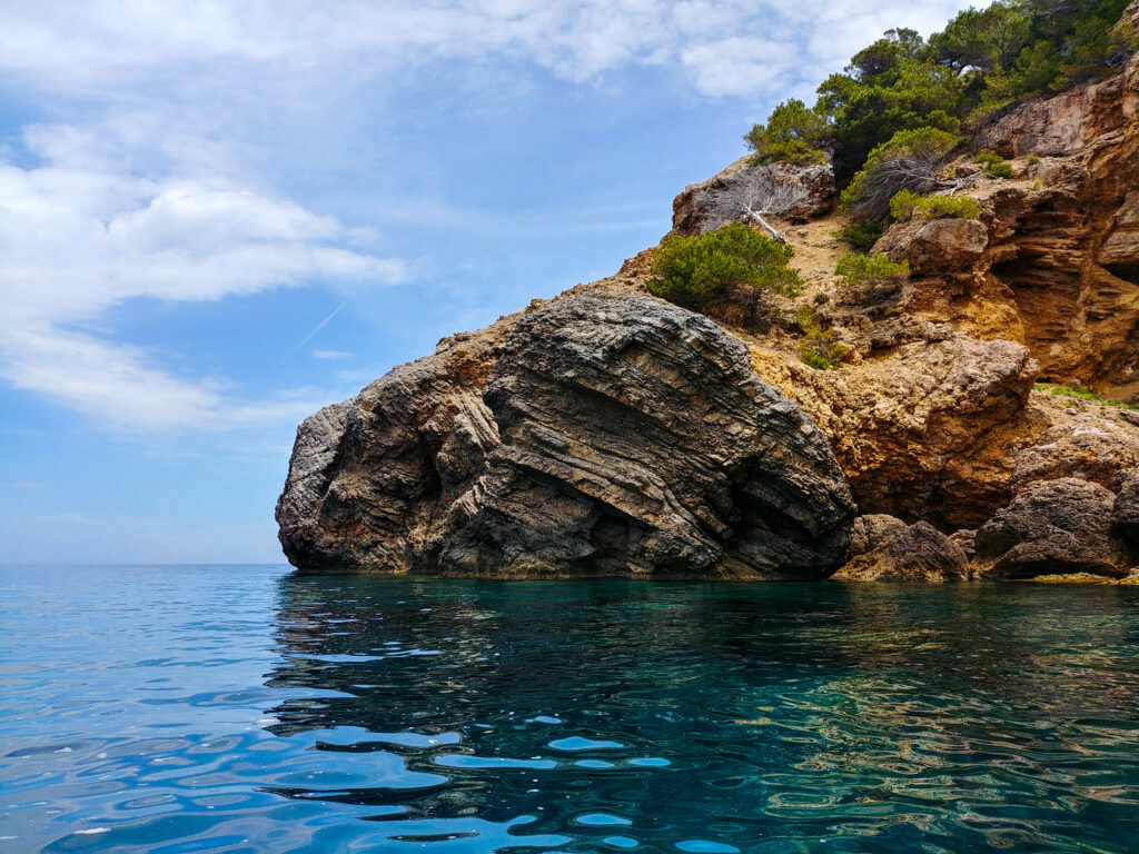 Dramatic coastal cliff with rugged rocks green bushes and vivid blue sea under cloudy sky wallpaper
