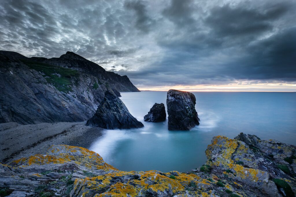 Dramatic coastal cliffs with yellow lichen over blue sea beneath moody clouded sky wallpaper background