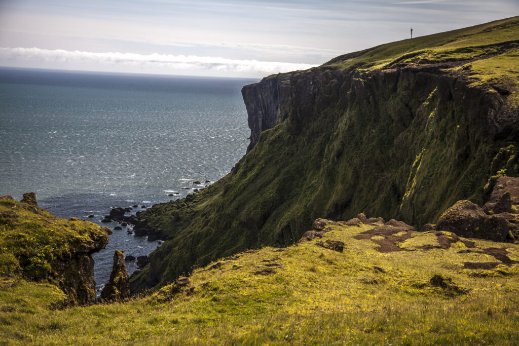Dramatic coastal cliffs with lush green grass rugged shore rocks and deep blue sea horizon wallpaper