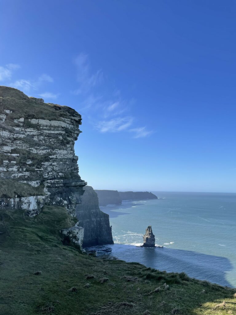 Dramatic coastal cliffs with layered rocks vibrant green grass and deep blue ocean horizon wallpaper