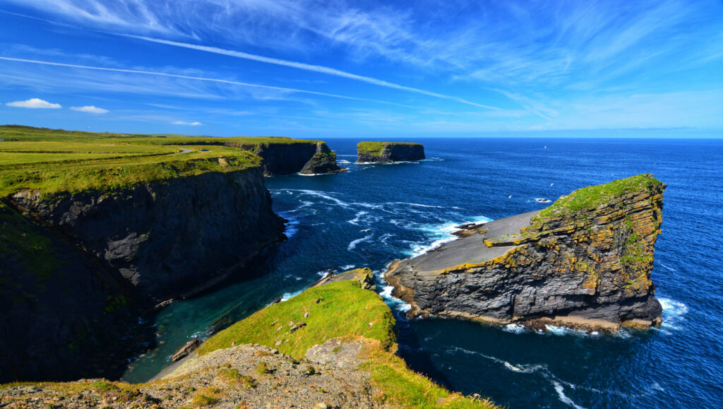 Dramatic coastal cliffs with jagged rocks and foaming waves under a bright blue sky wallpaper