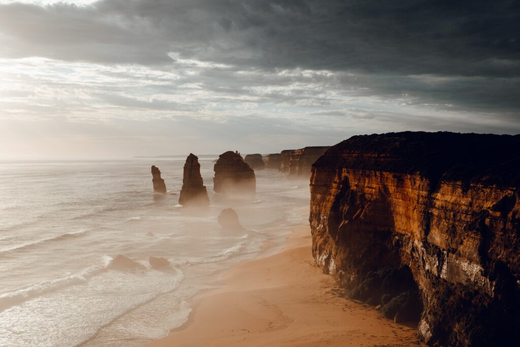 Aerial view of dramatic coastal cliffs rock formations ocean waves and golden sandy shore wallpaper