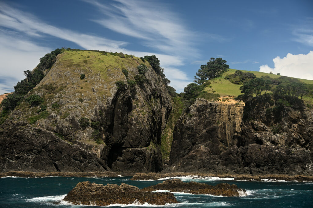 Dramatic cliffs and hills rise from sea with dark rocks foamy shore lush greenery vivid sky wallpaper
