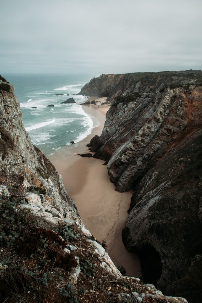 Dramatic coastal cliffs with sandy beach muted gray tones serene overcast sky wallpaper background