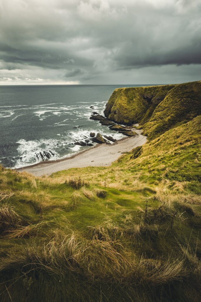 Dramatic coastal cliffs with green grass overlooking calm sea and waves on a secluded beach Wallpaper
