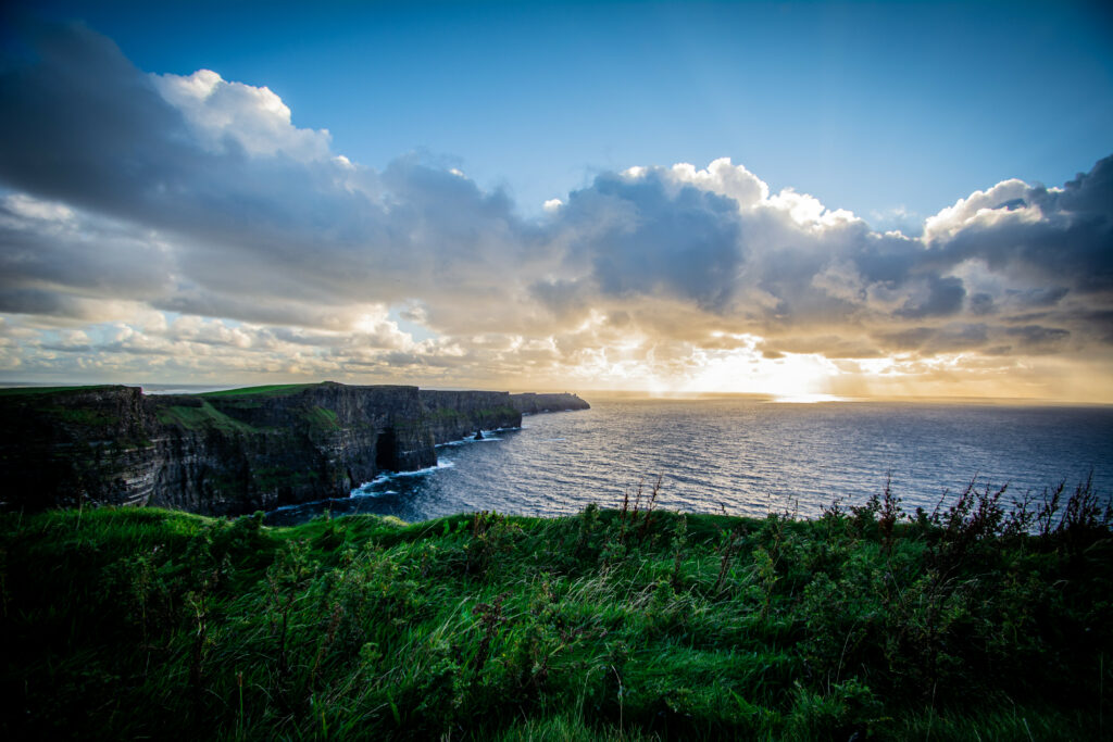 Dramatic coastal cliffs with rocky shores and green grass under soft sunlight and cloudy sky wallpaper