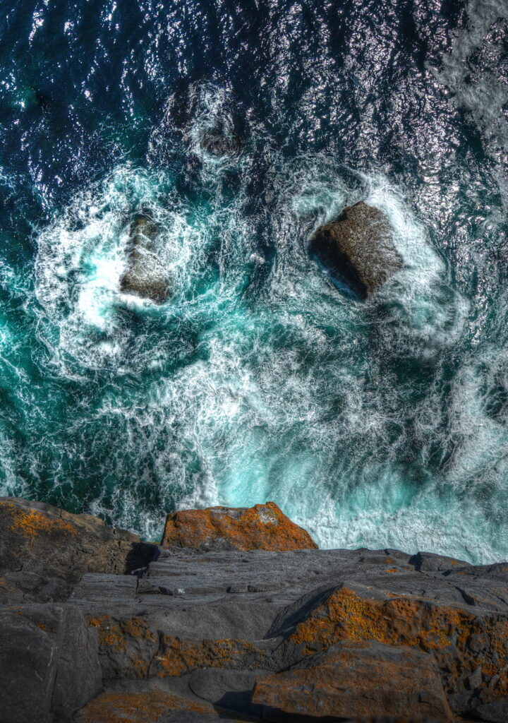 Aerial view of rugged rocks and crashing waves on a dramatic deep blue coastline wallpaper