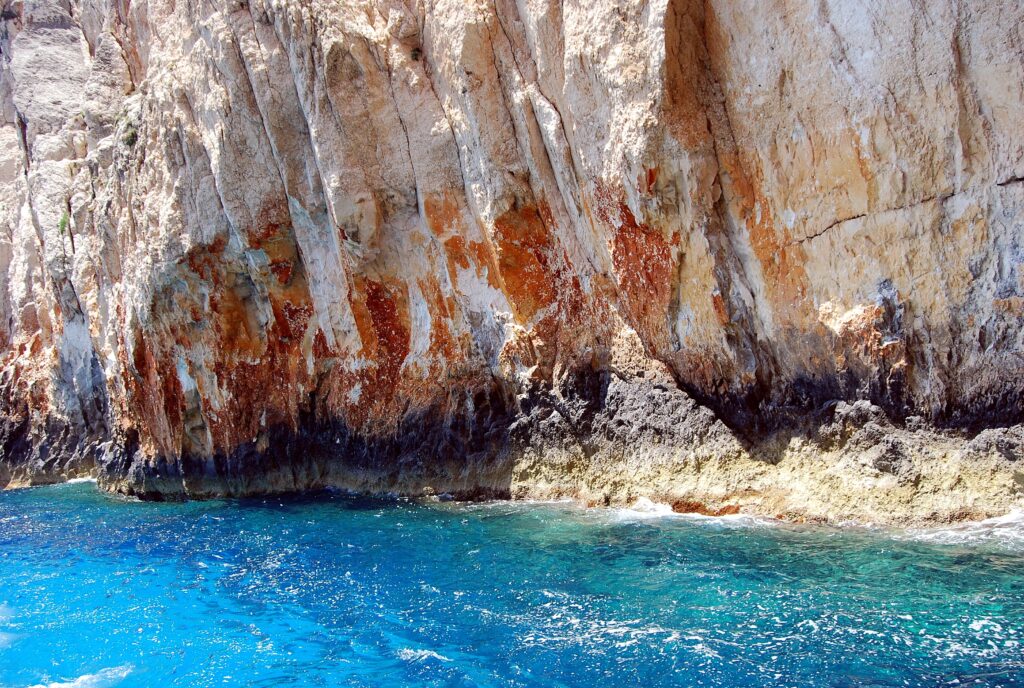 Dramatic coastal wallpaper with deep blue sea and textured rugged stone cliffs layers