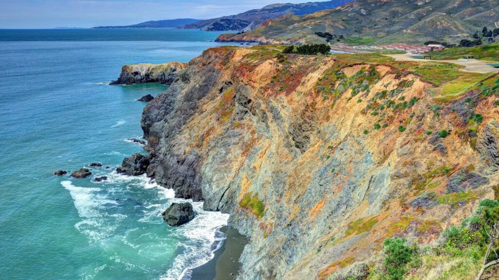 Dramatic coastal cliffs with green grass and rugged rocks overlooking deep blue sea waves Wallpaper