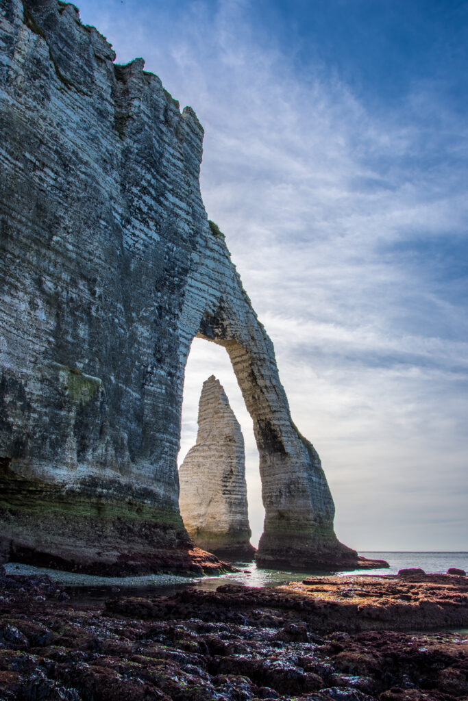 Dramatic coastal cliffs with natural stone arch opening to serene beach and calm blue sea wallpaper