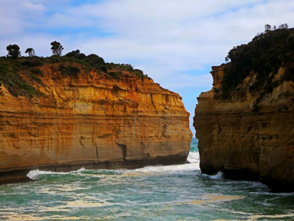 Dramatic coastal cliffs with orange and brown layers framing foaming sea under cloudy sky wallpaper