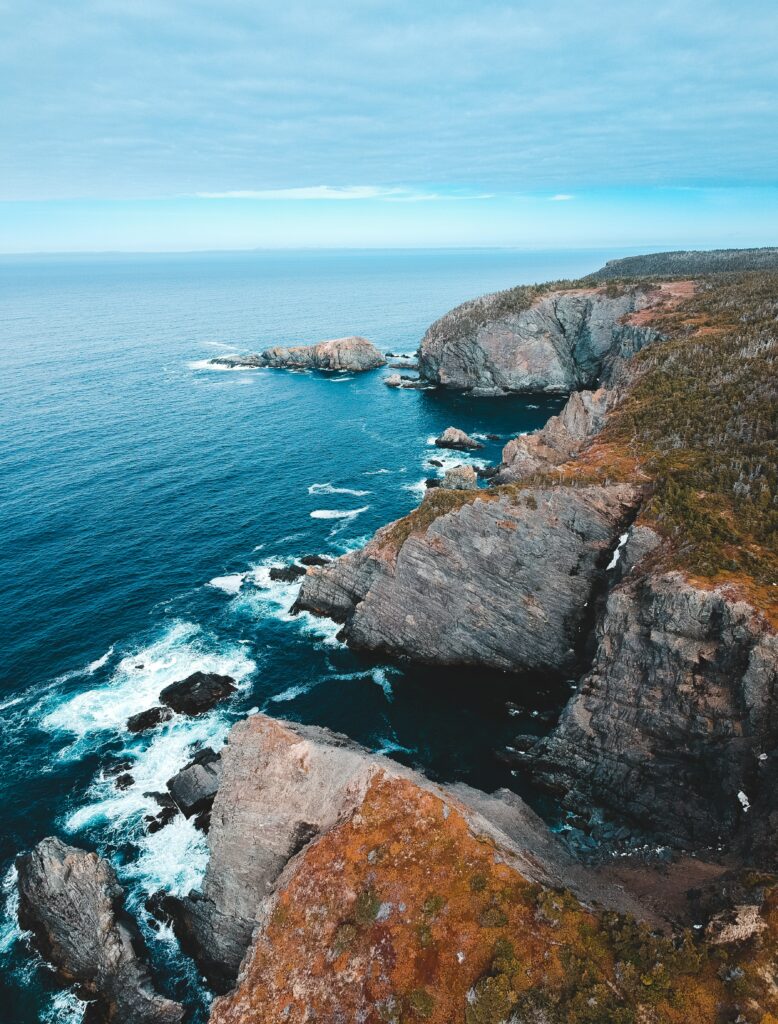 Dramatic coastal cliffs with rugged rocks and foamy waves under a cloudy sky ocean wallpaper