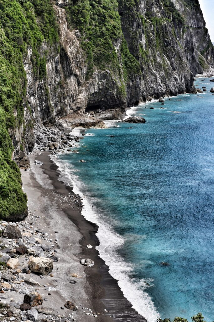 Dramatic coastal cliffs with lush greenery turquoise sea and foamy waves on rocky shore wallpaper