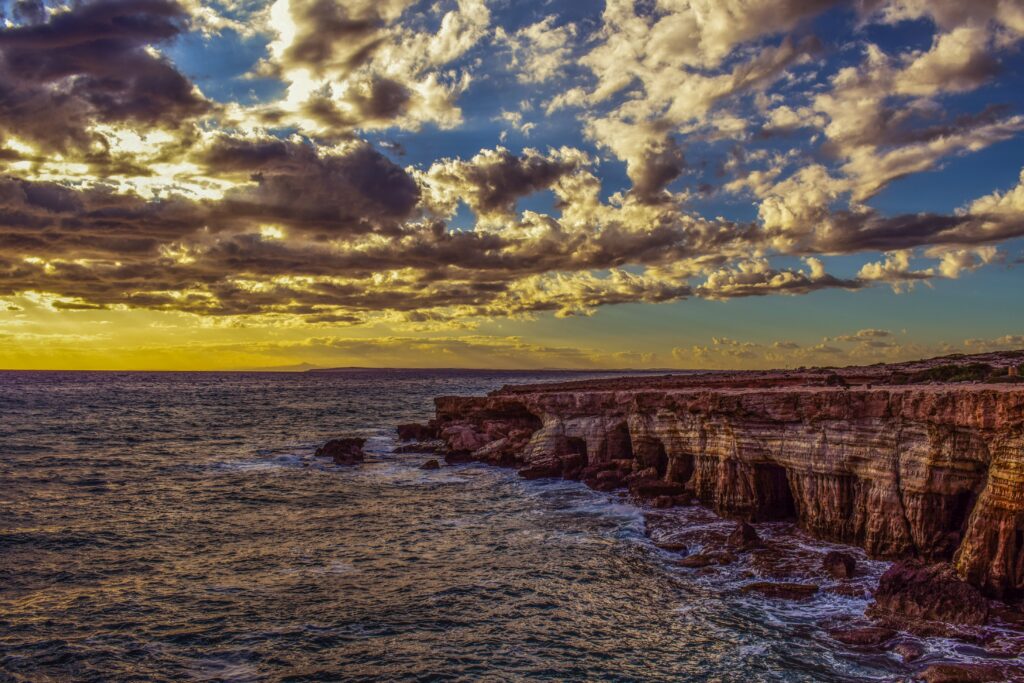 Dramatic coastal cliffs with vibrant stones and golden HDR sky over restless sea wallpaper background