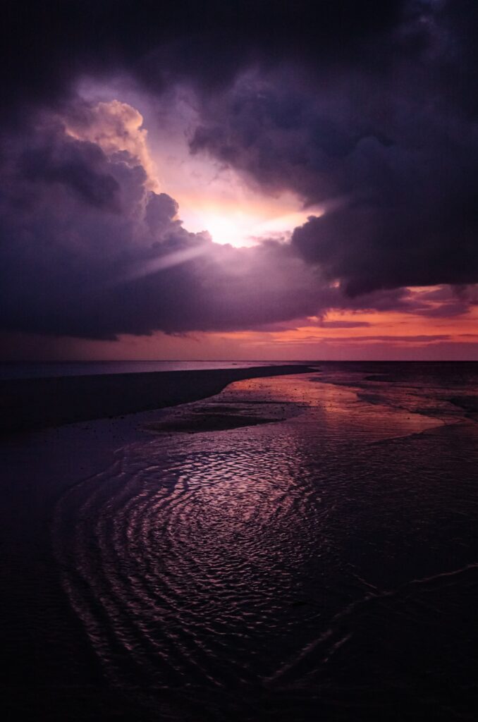 Dramatic coastal sunset with purple pink skies reflecting on wet sands and calm ocean waves Wallpaper