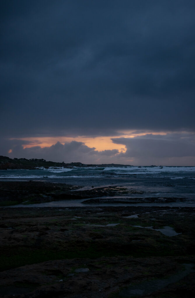 Dramatic coastal wallpaper at dusk with rugged rocks deep blue sea waves and moody sky background