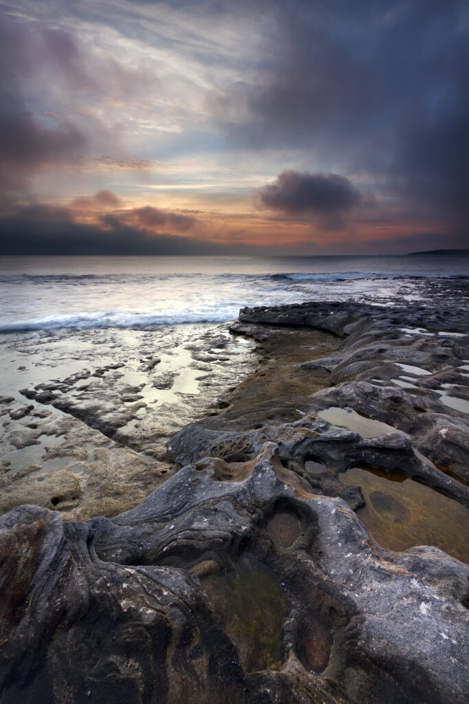 Dramatic coastal landscape with rugged stones tidal pools and colorful evening sky wallpaper background