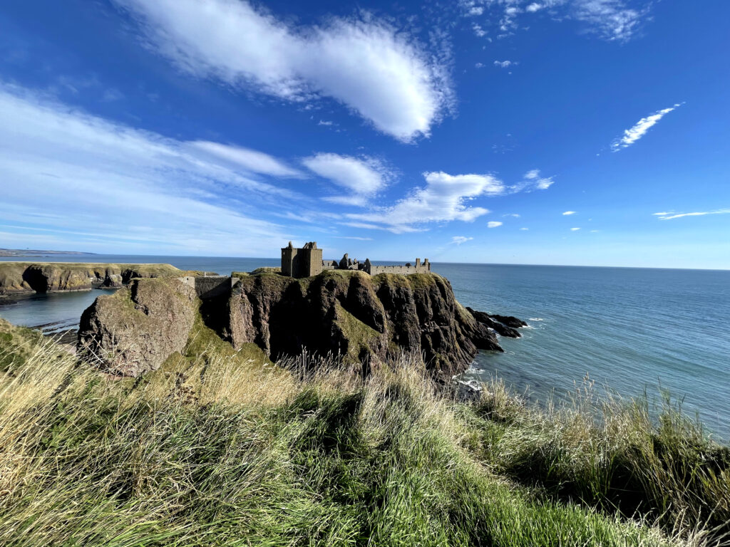 Dramatic coastal fortress on rugged cliffs overlooking vast blue sea under vibrant sky wallpaper
