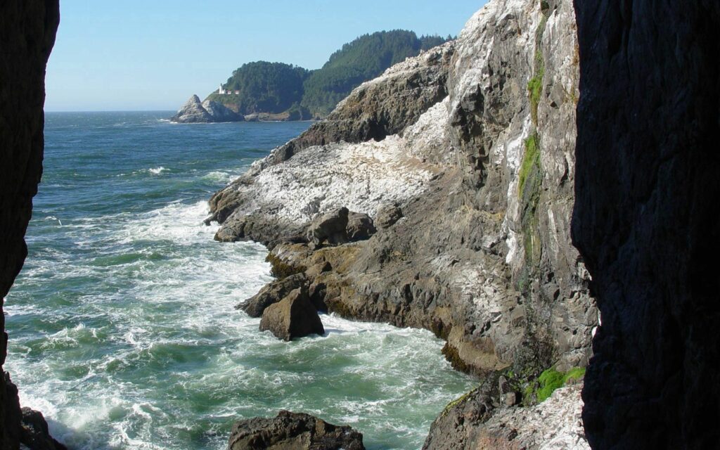 Dramatic coastal wallpaper with rugged rocks crashing waves and sunlit gorge entrance background