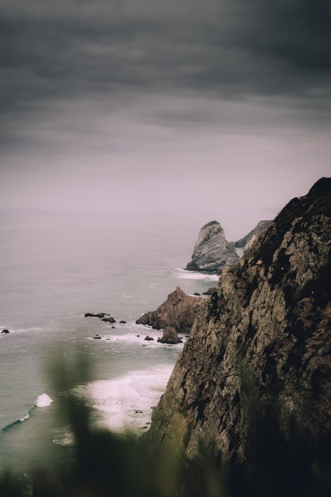 Dramatic coastal cliffs with rugged rocks and calm sea under moody overcast sky wallpaper background