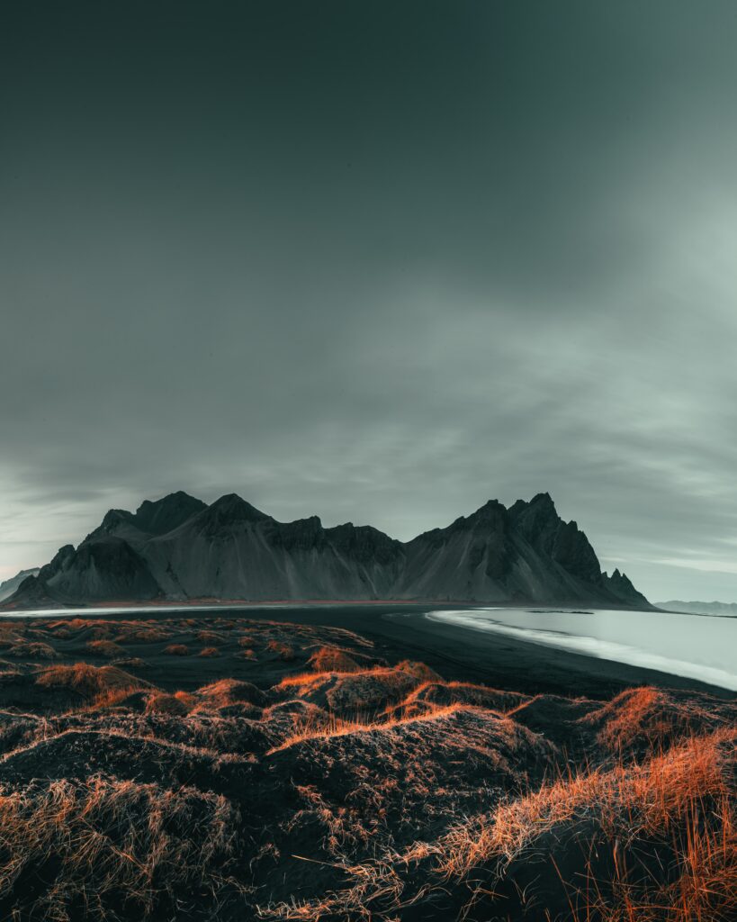 Dramatic coastal landscape wallpaper with rugged mountains orange grasses and moody sky background