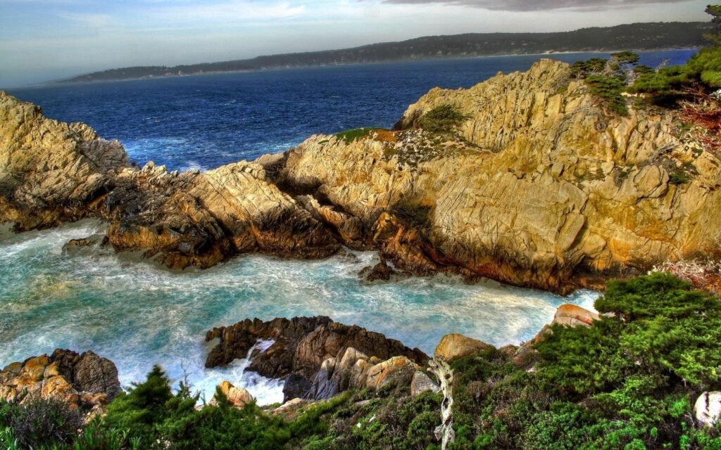 Dramatic coastal landscape with rugged cliffs waves crashing lush greenery and deep blue sea Wallpaper