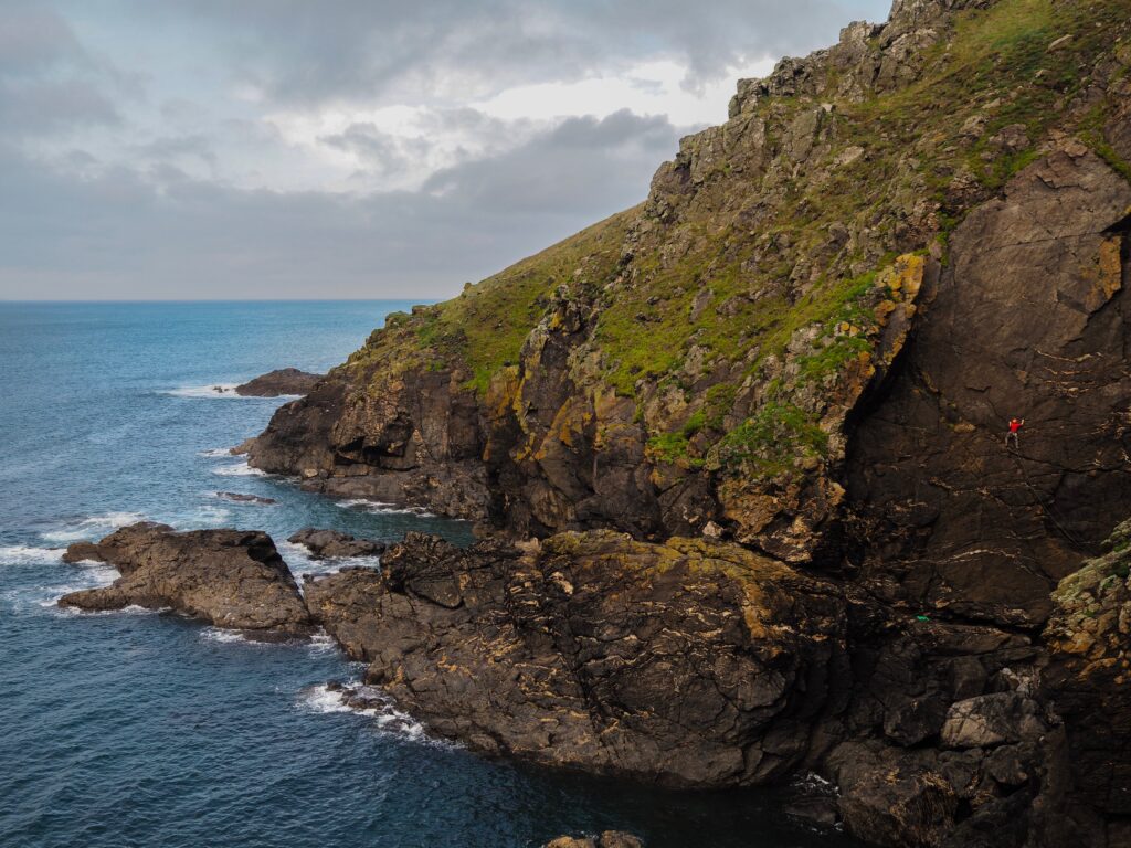 Dramatic coastal landscape with rugged rocks foamy waves and green grass by vibrant blue sea Wallpaper