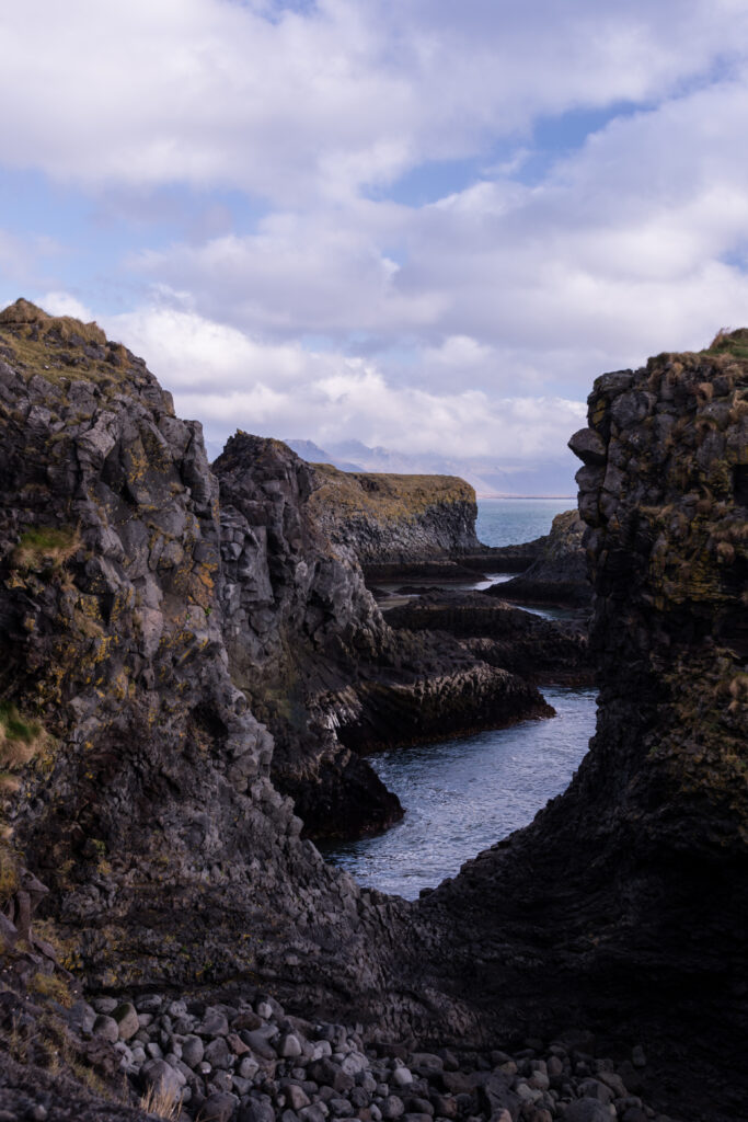 Dramatic coastal landscape with rugged cliffs mossy rocks and calm water under cloudy sky wallpaper