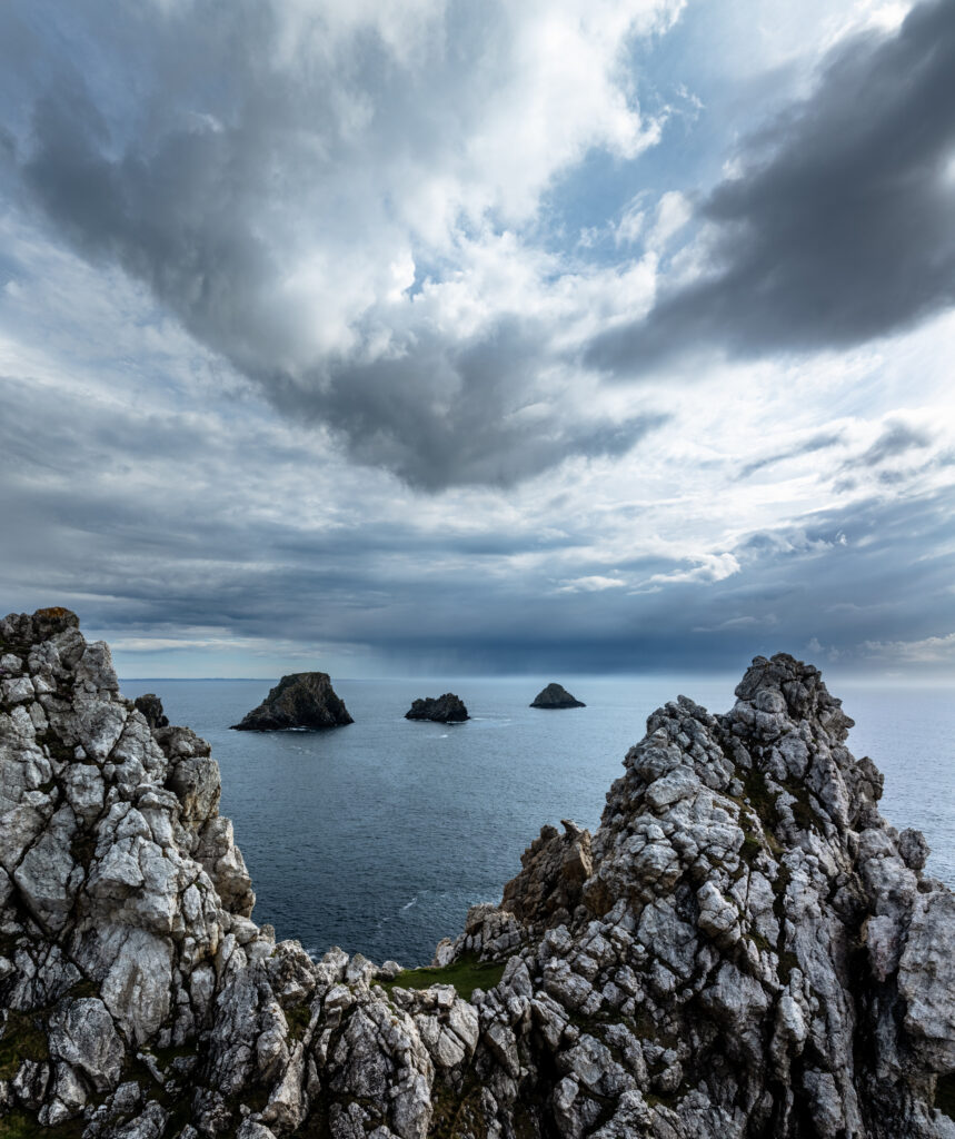 Rugged white rocks framing dramatic blue bay with distant islets under moody cloudy sky wallpaper