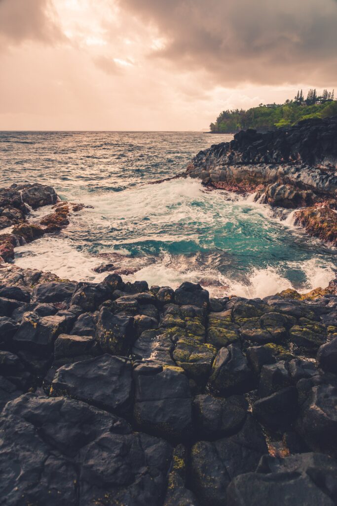 Dramatic coastal landscape with black rocks foaming waves and moody cloudy sky wallpaper background