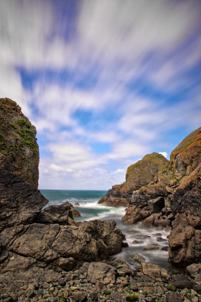 Dramatic coastal landscape with rugged rocks and dynamic clouds over vibrant blue sky wallpaper