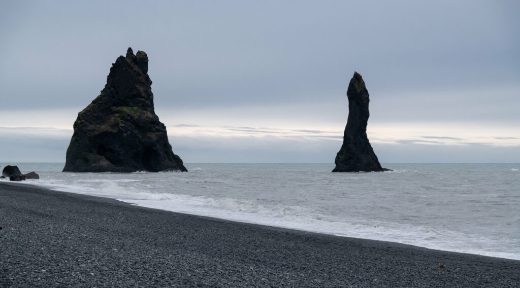 Dramatic coastal landscape with towering sea rocks moody sky and gentle waves on pebbled shore Wallpaper