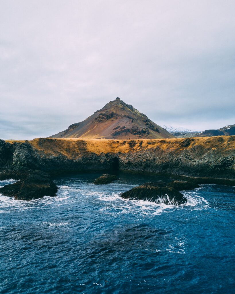 Rugged hill with golden grasses dark rocks and deep blue sea under cloudy sky coastal wallpaper background