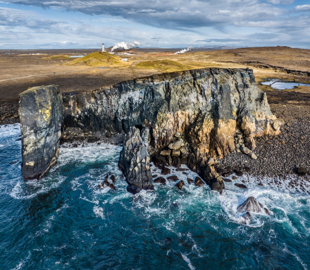 Dramatic coastal landscape with rugged rocks and solitary lighthouse under cloudy sky wallpaper