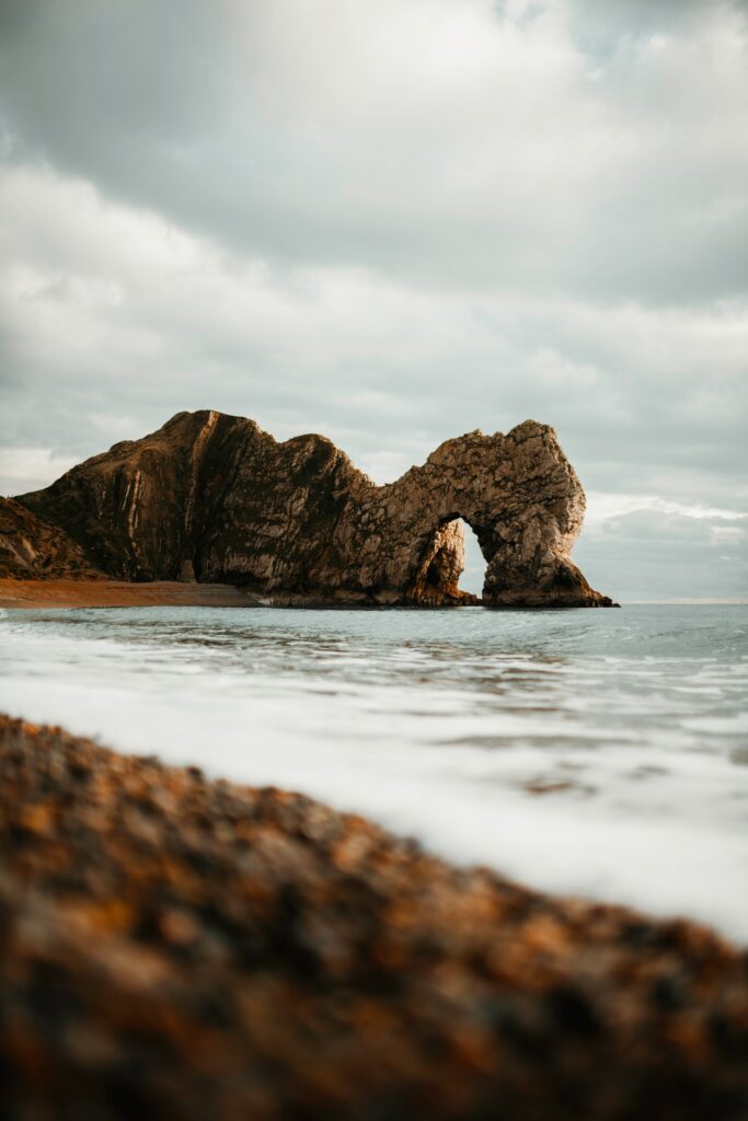 Natural rock arch on rugged shoreline with weathered rocks gentle waves and dramatic sky wallpaper