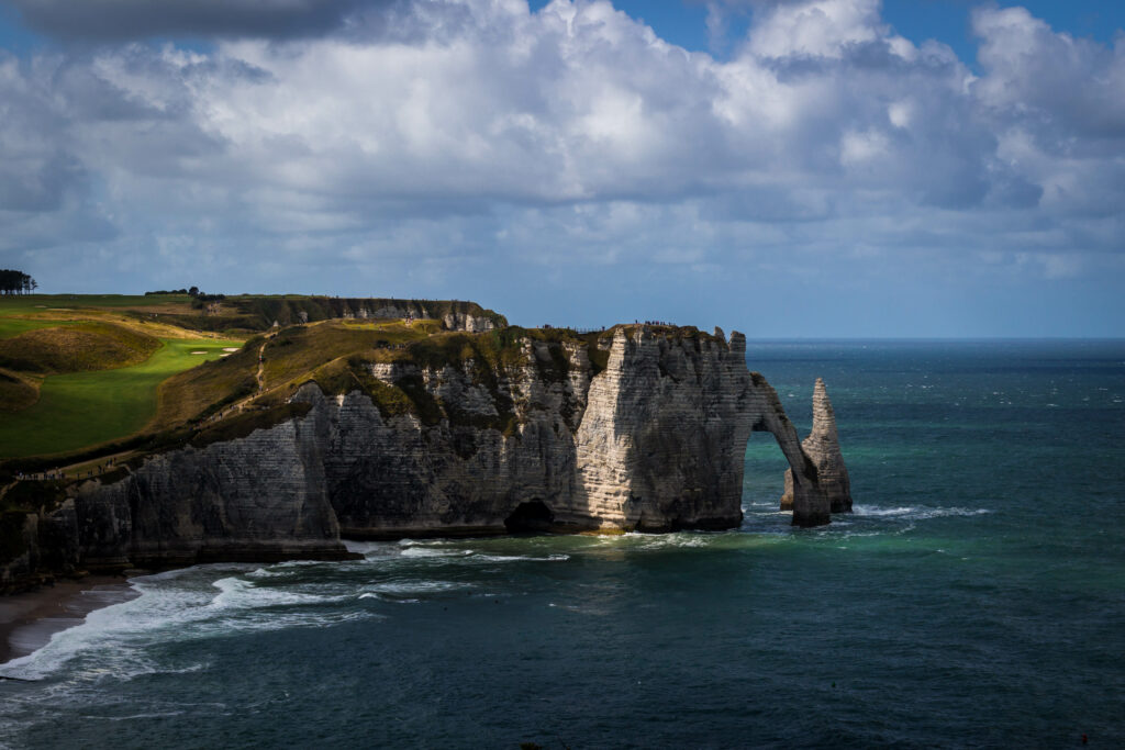 Dramatic coastal landscape with towering rock arch rugged cliffs lush greenery and crashing waves Wallpaper