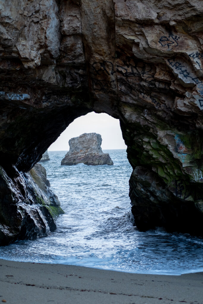 Natural rock arch framing rugged sea stack with ocean waves and graffiti coastal landscape wallpaper