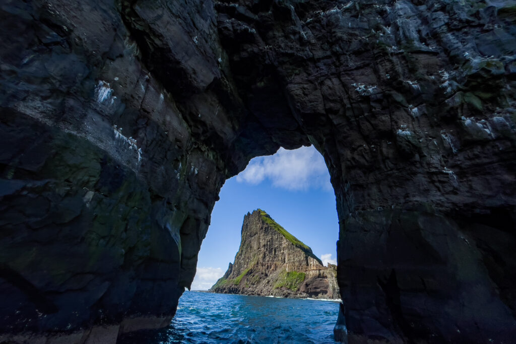 Natural rock arch framing sea stack with vibrant blue waters and lush green coastal cliffs wallpaper