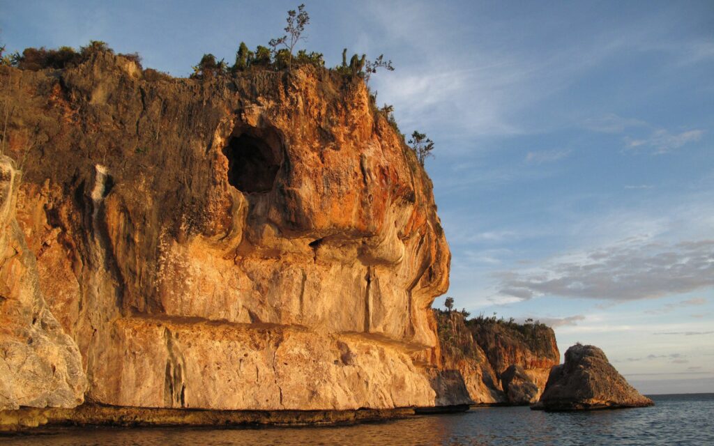 Dramatic coastal rock formation with large hole illuminated by sunlight over calm waters wallpaper